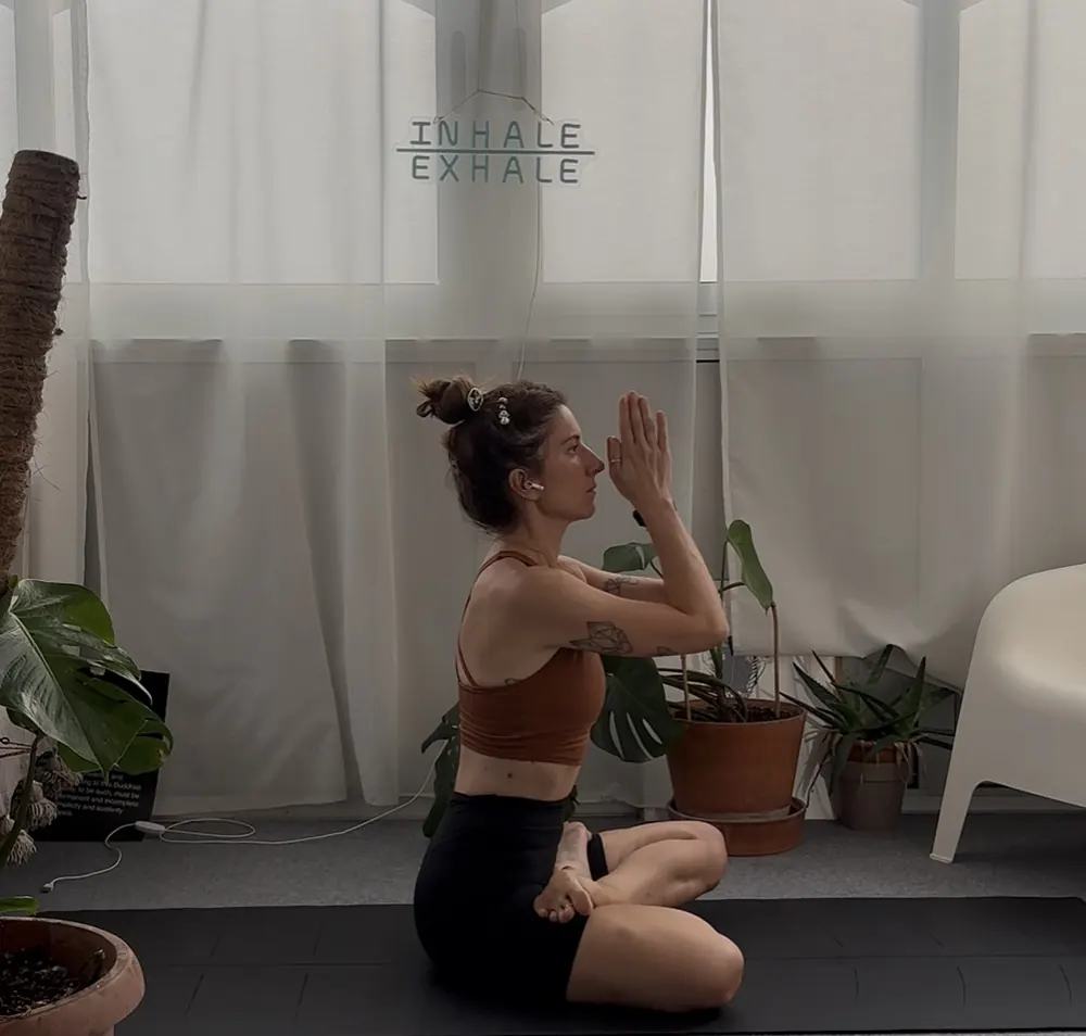 Roberta seduta sul tappetino, mani giunte davanti al viso, davanti a una finestra luminosa